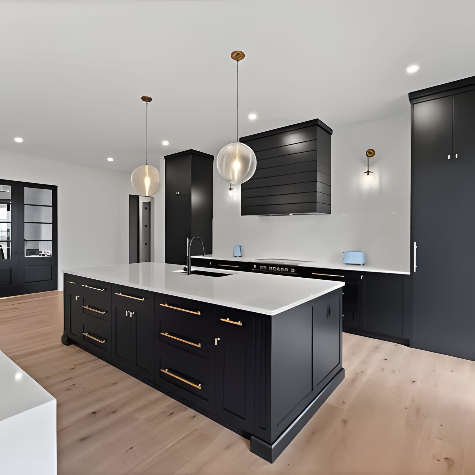 Black shaker cabinets with slim brass pulls, white stone counters, and pale oak floors keeping it light.