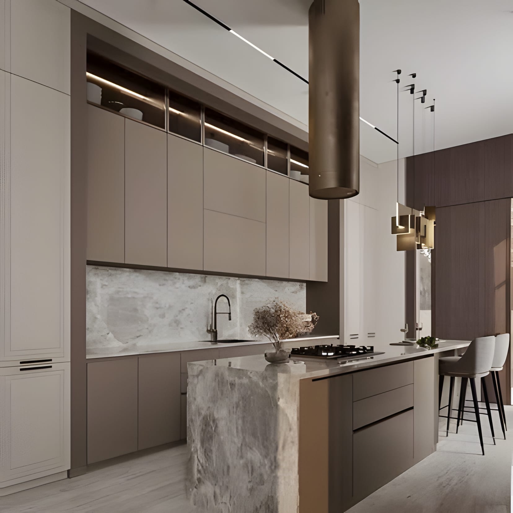 A tall bronze hood column over a stone waterfall island, taupe cabinetry keeping the room warm.