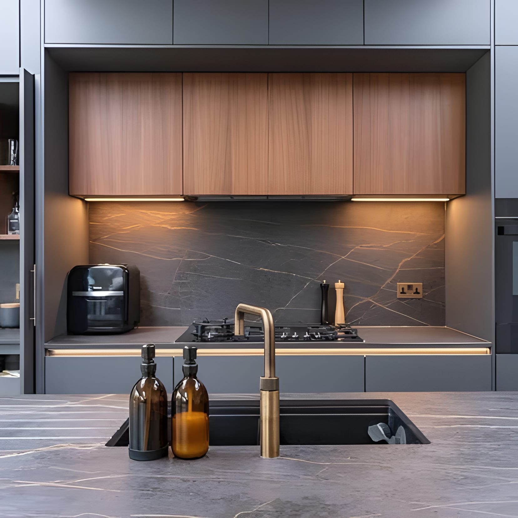Blue-grey cabinetry, a wood shelf under the hood, and a brass tap over dark stone.