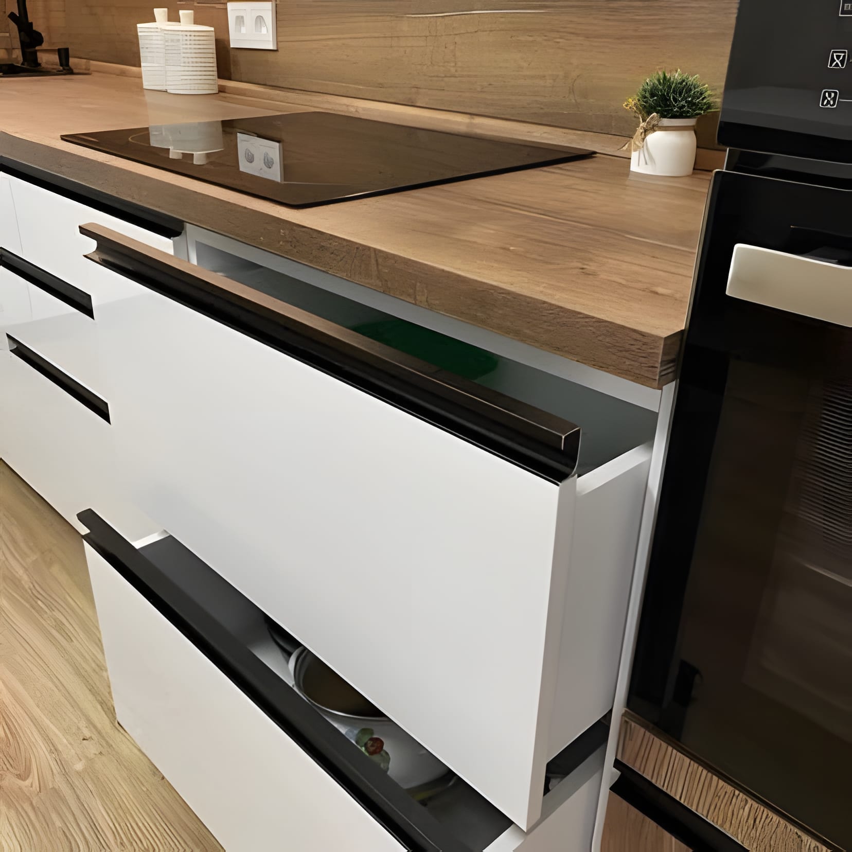 White drawers under a thick oak worktop with a black induction hob set flush — a close-up worth keeping.