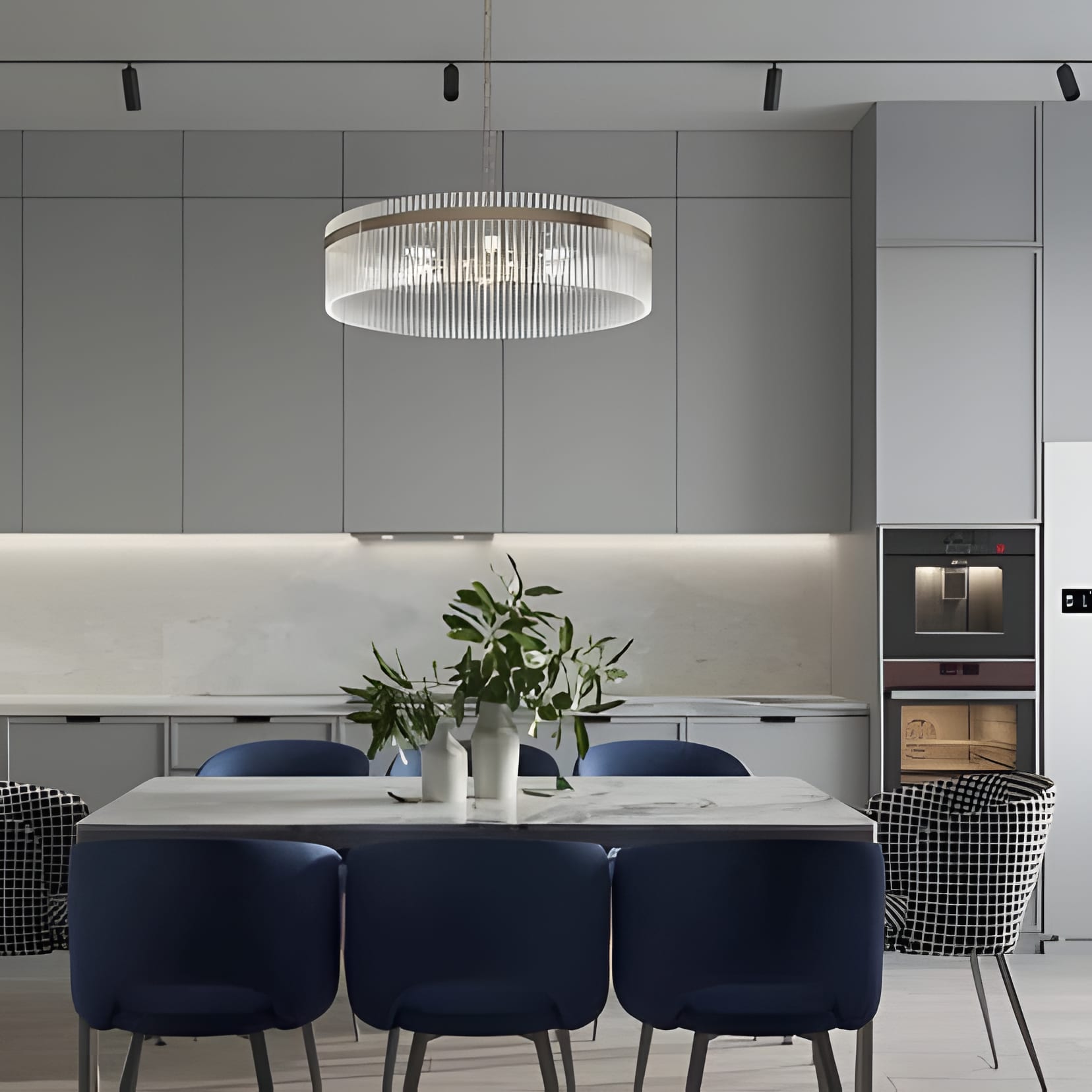 A grey kitchen with a drum chandelier and six navy velvet chairs around the dining table.