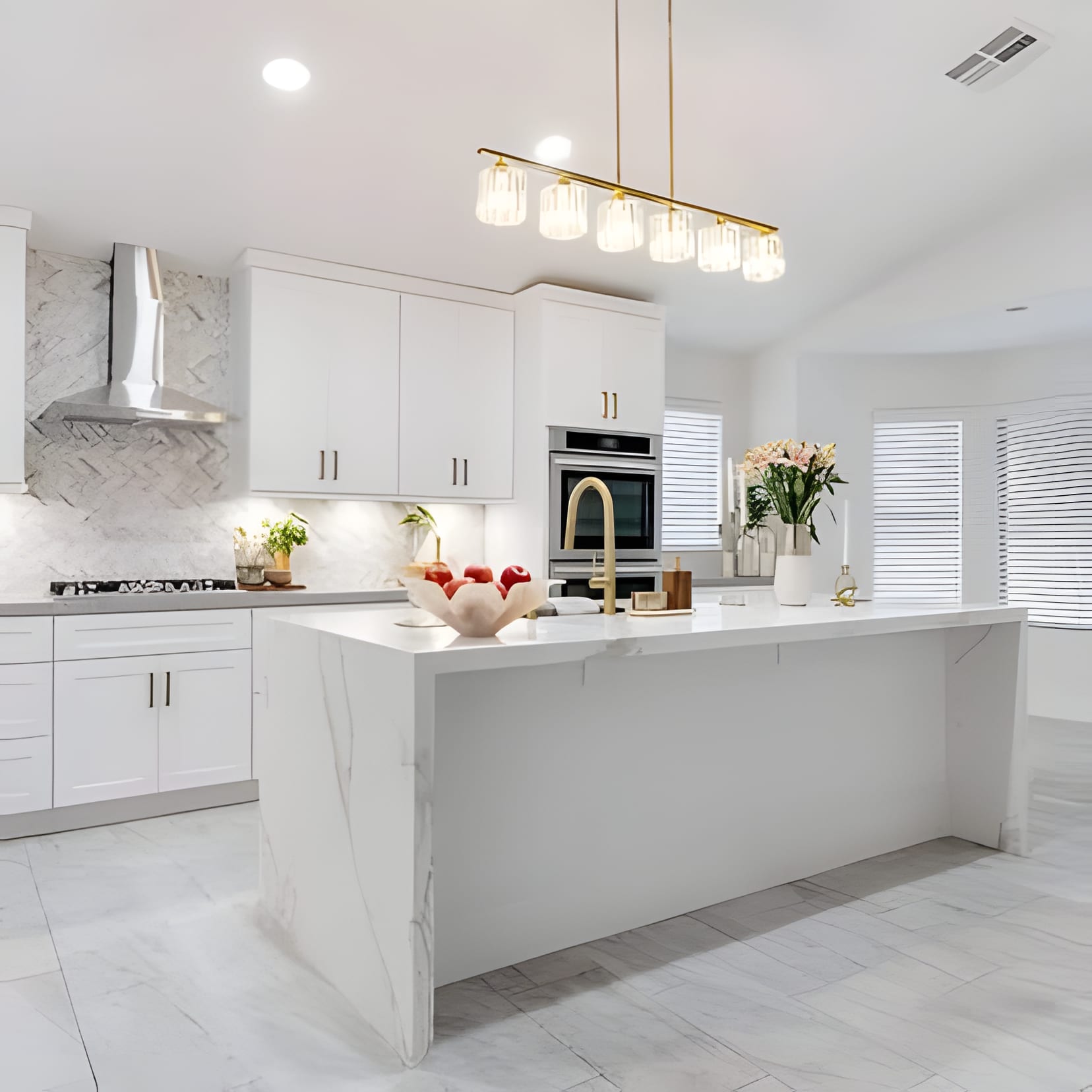 A white shaker kitchen under a vaulted ceiling, a brass rail light over the island and flowers everywhere.