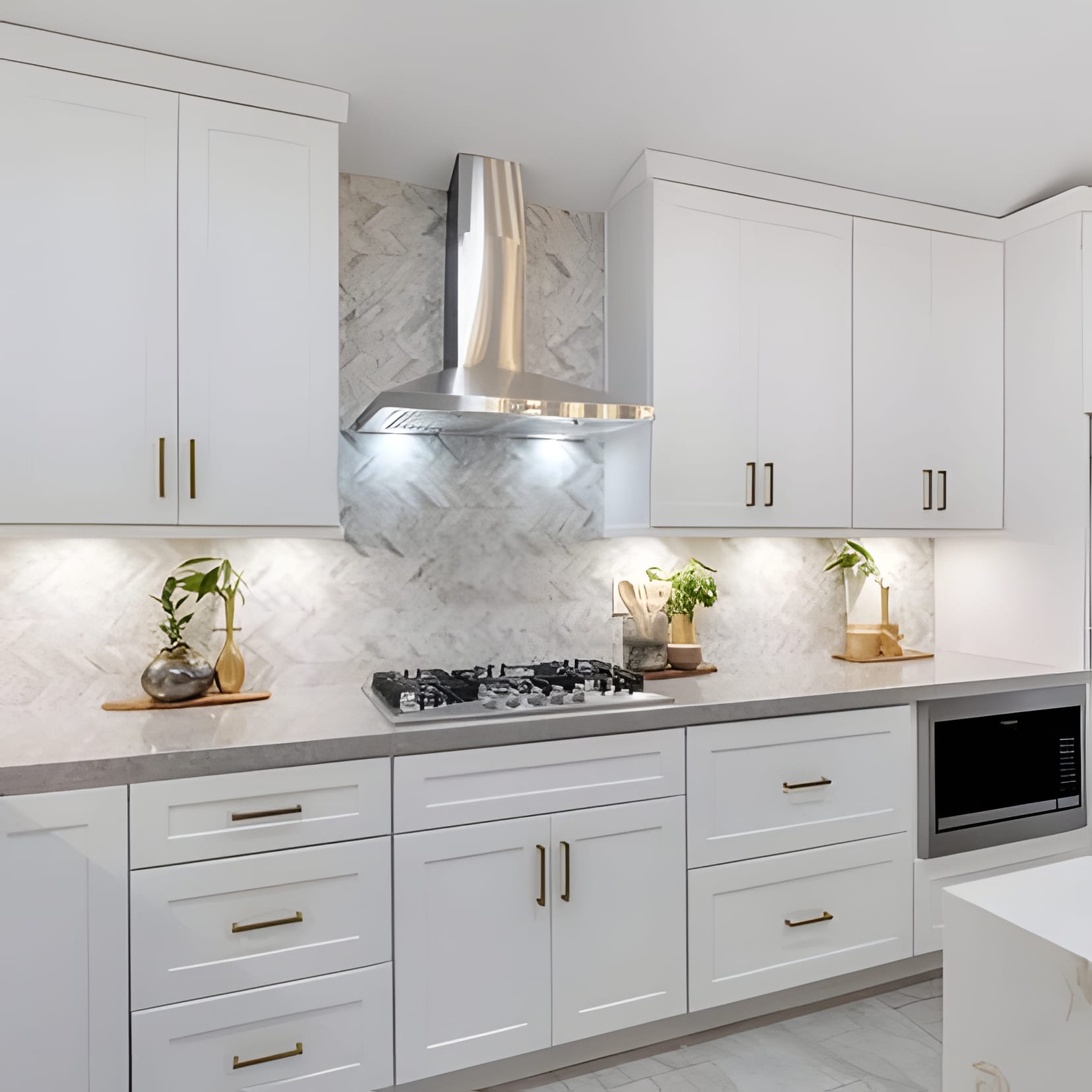 A white shaker kitchen with a steel hood and pots of herbs along the marble splash.